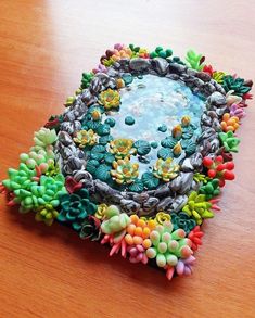 a bowl filled with lots of different colored flowers on top of a wooden table next to a water fountain