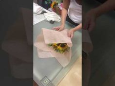 a woman is wrapping flowers on top of a table in an office setting with sunflowers