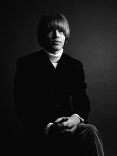 a black and white photo of a man in a suit sitting on a chair with his legs crossed