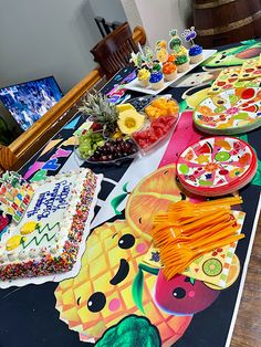 the table is covered with many colorful plates and food items, such as pizzas, pineapples, fruit, and watermelon slices