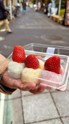 a person holding a plastic container filled with pastries and strawberries on top of it