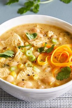 a white bowl filled with chicken and vegetable soup on top of a table next to cilantro