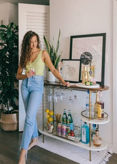 a woman standing in front of a bar with bottles and glasses on the shelf next to her