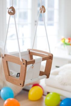 a wooden baby swing hanging from the ceiling in a child's room with colorful balls