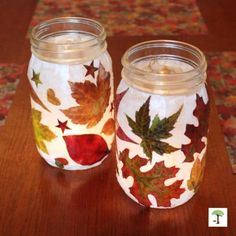 two glass jars with autumn leaves painted on them sitting on a wooden table next to a rug