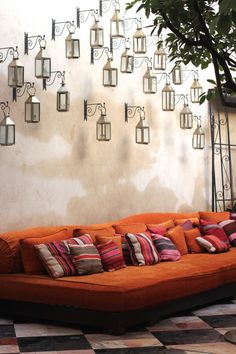 an orange couch sitting in front of a wall with lots of hanging lanterns on it