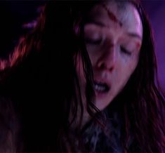 a woman with her eyes closed and blood smeared all over her face, standing in front of a purple background