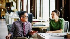 two people sitting at a table in an office setting talking to each other and discussing