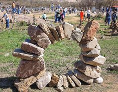 a group of people standing around rocks stacked on top of each other in the grass