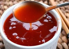 a spoon full of sauce being poured into a white cup with chopsticks next to it