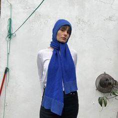 a woman standing in front of a white wall wearing a blue scarf