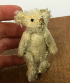 a small teddy bear sitting on top of a wooden table next to a person's hand