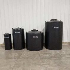 three black tanks sitting next to each other on the floor in front of a white wall