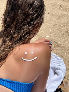 a woman with a smiley face painted on her arm and chest sitting in the sand