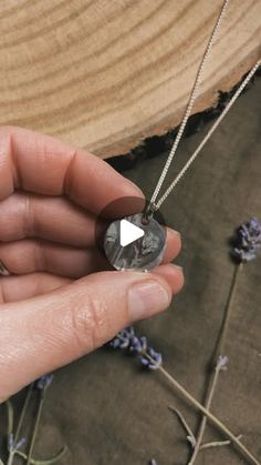 a person holding a piece of jewelry in their hand with lavender flowers around it and a wooden background