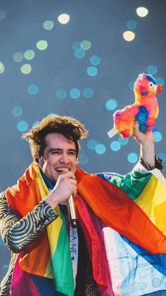 a man holding a stuffed animal in his right hand and wearing a rainbow scarf around his neck