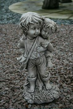 a statue of two little boys hugging each other on top of some rocks and gravel