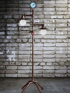 a lamp that is sitting on top of a metal stand in front of a brick wall