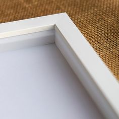 an empty white frame sitting on top of a brown cloth covered floor with a cat laying in the corner