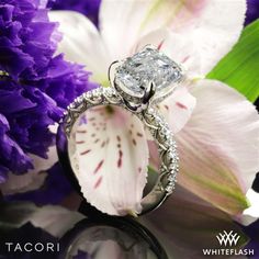 a diamond ring sitting on top of a flower next to purple and white flowers with the words tacori written below it