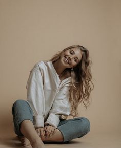 a woman sitting on the floor with her hair blowing in the wind and smiling at the camera