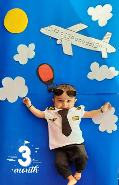 a young boy wearing sunglasses and a tie laying on top of a blue backdrop with an airplane