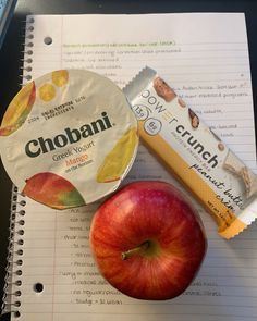 an apple, candy bar and chocolate chip on top of a notebook