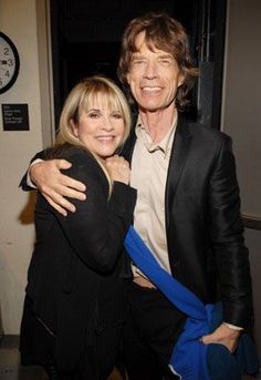 a man and woman hugging each other in front of a wall with a clock on it