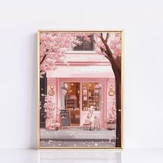 a framed photograph of a storefront with pink flowers on the trees and chairs in front