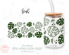 a glass jar with a straw in the middle and green leaves on it, next to a