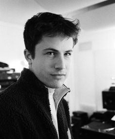 black and white photograph of a young man in a sweater looking at the camera with serious expression on his face