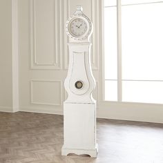 a white grandfather clock sitting on top of a hard wood floor next to a window