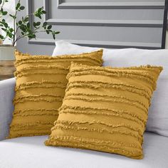 two yellow pillows sitting on top of a white couch next to a potted plant