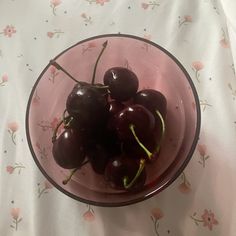 a glass bowl filled with cherries on top of a floral tablecloth covered table