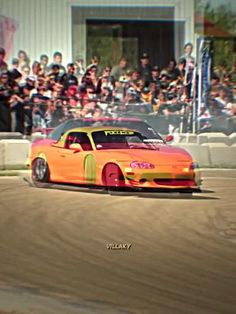 an orange sports car driving around a track in front of a group of people watching