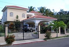 a car is parked in front of a house that has a gated driveway and palm trees