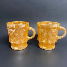 two yellow glass mugs sitting next to each other on a gray surface with black background