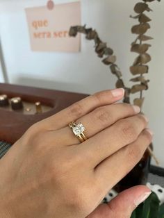 a woman's hand with a ring on it and a plant in the background