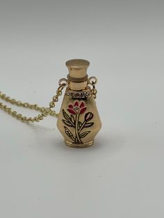 a small gold vase with flowers painted on it's side is sitting on a chain