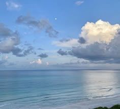 an ocean view with clouds in the sky and some water on the beach near by