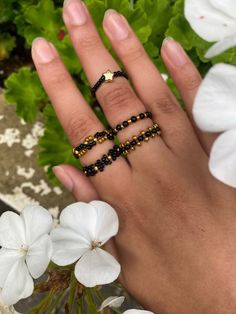 a woman's hand with three rings on it and flowers in the foreground