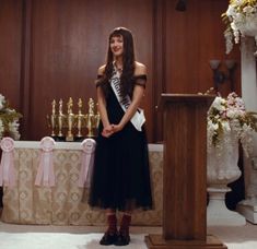 a woman standing at a podium in front of flowers and candles on the wall behind her