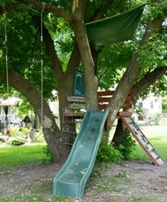 a green slide in the middle of a tree next to a swing set and some trees