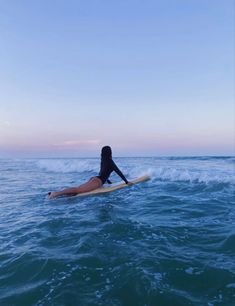 a woman is laying on her surfboard in the middle of the ocean at sunset