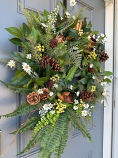 a wreath with pine cones, evergreens and other greenery hangs on the front door