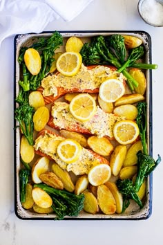 a pan filled with fish, potatoes and broccoli on top of a table