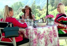 three women sitting at a table with plates and glasses on it, talking to each other