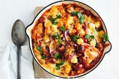 a casserole dish with meat and vegetables on a cutting board next to a spoon