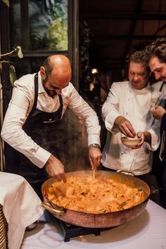 three men in chef's uniforms are preparing food on a table with white linens