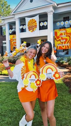 two girls in orange dresses holding up signs and smiling at the camera while standing on grass